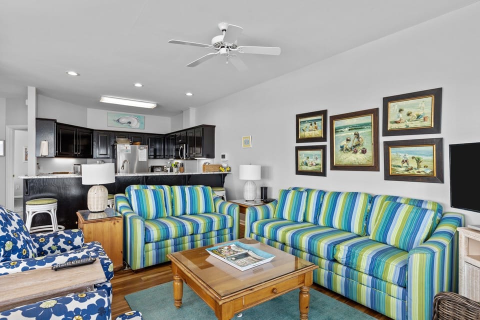 Relax in this bright coastal living space with vibrant striped sofas, open kitchen, and charming beach-themed artwork adorning the walls.