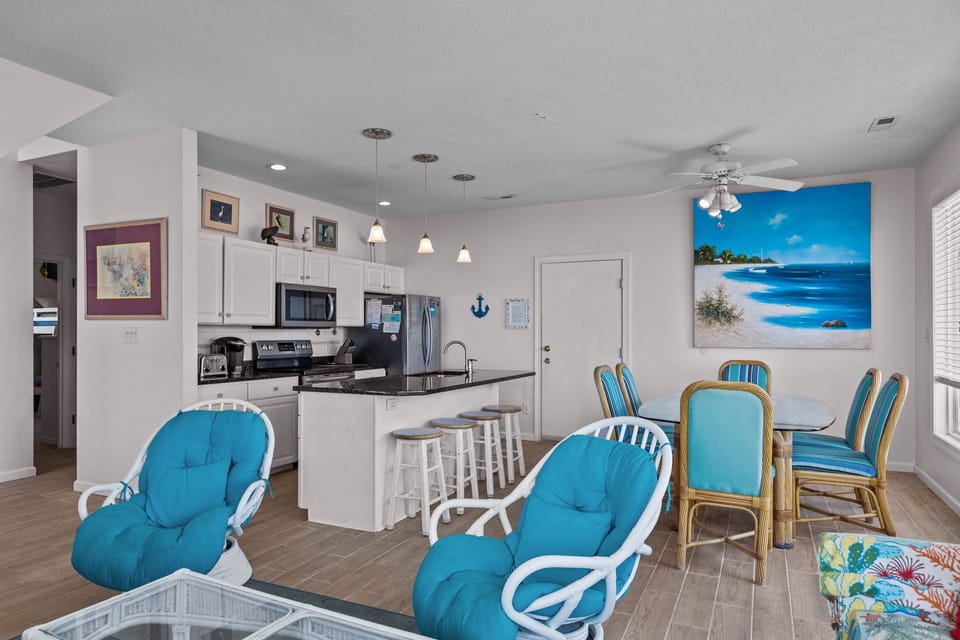 Your bright coastal retreat blends modern kitchen convenience with beachy comfort—where ocean artwork and turquoise accents make every meal feel like vacation.
