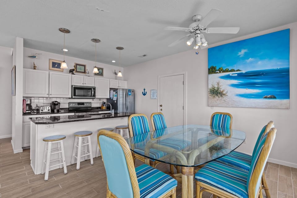 Your open-concept kitchen flows into a bright dining area, where tropical-themed seating and ocean artwork create a breezy coastal vibe for memorable meals.
