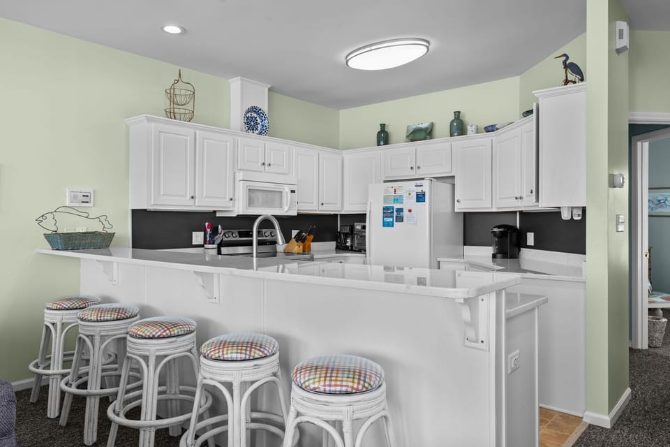 Your fully equipped kitchen awaits with white cabinets, breakfast bar seating, and everything needed for memorable meals together.