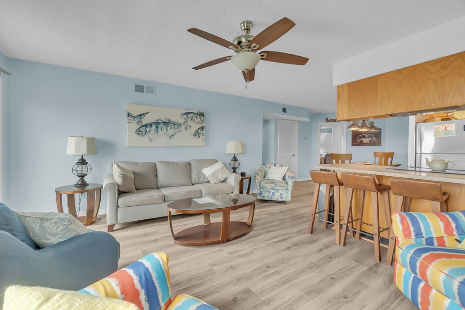 Relax in your bright, coastal-themed living space with comfortable seating, ocean-inspired decor, and an open kitchen perfect for vacation meal prep.