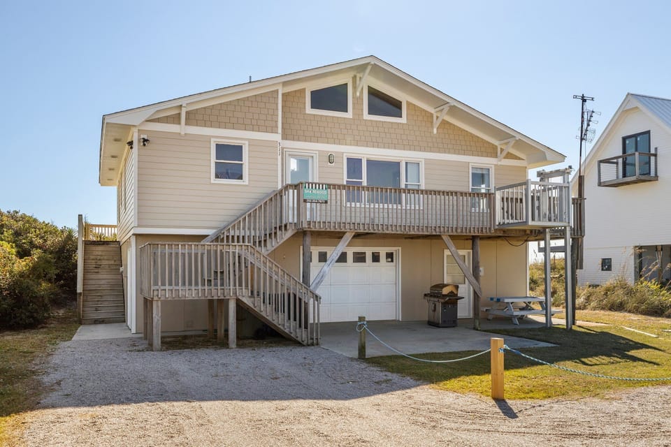 Coastal beach house with elevated deck and covered parking area, situated in a quiet residential neighborhood.