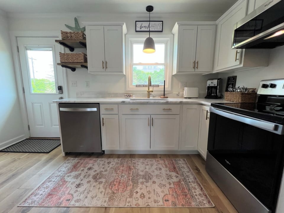Your bright, modern kitchen features white cabinetry, stainless steel appliances, and cozy coastal touches perfect for preparing home-cooked meals during your getaway.