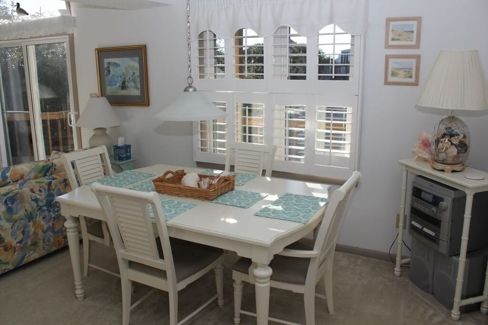 Your bright dining space features a charming white table where you'll share memorable meals, surrounded by coastal artwork and natural light.