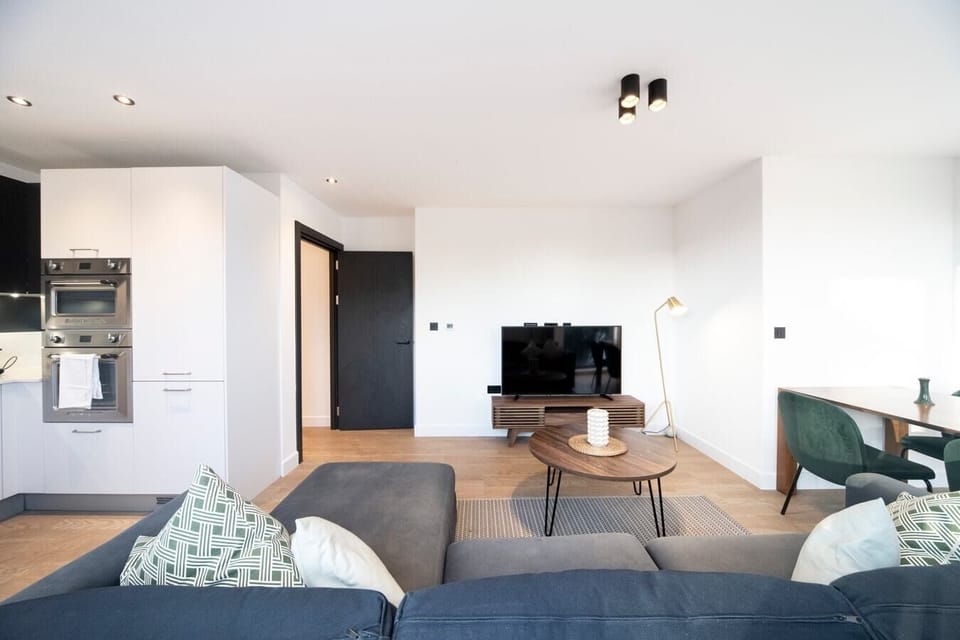 The bright living room features a pull-out sofa bed, a Smart TV, a dining table and chairs, and a small balcony