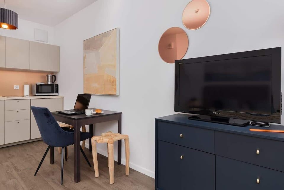 A dining and entertainment area with a TV stand, blue chairs, and a table set against a stylish backdrop.

