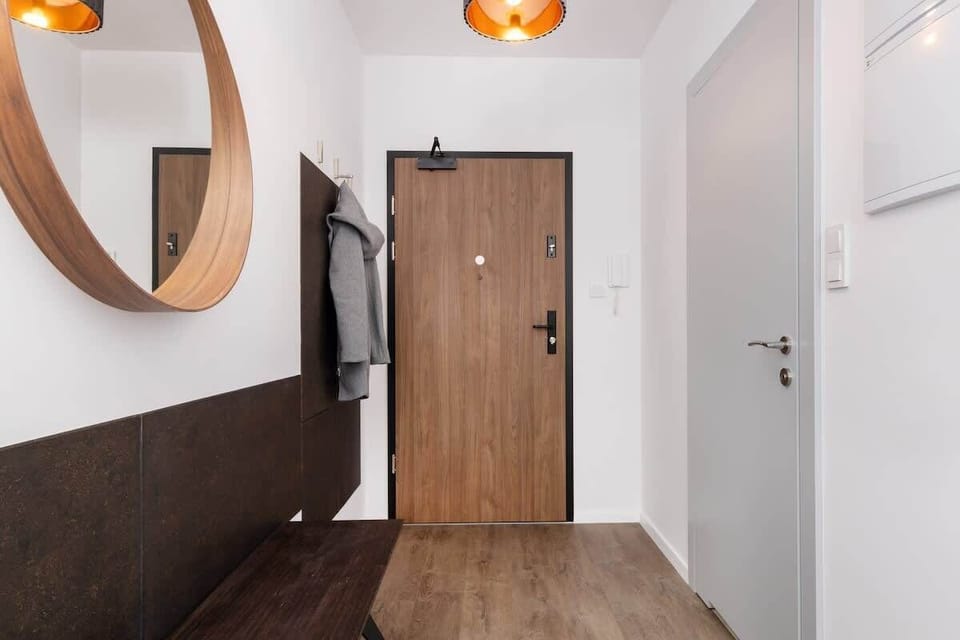 An entryway perspective showing a wooden door, a mirror, and a well-lit corridor.

