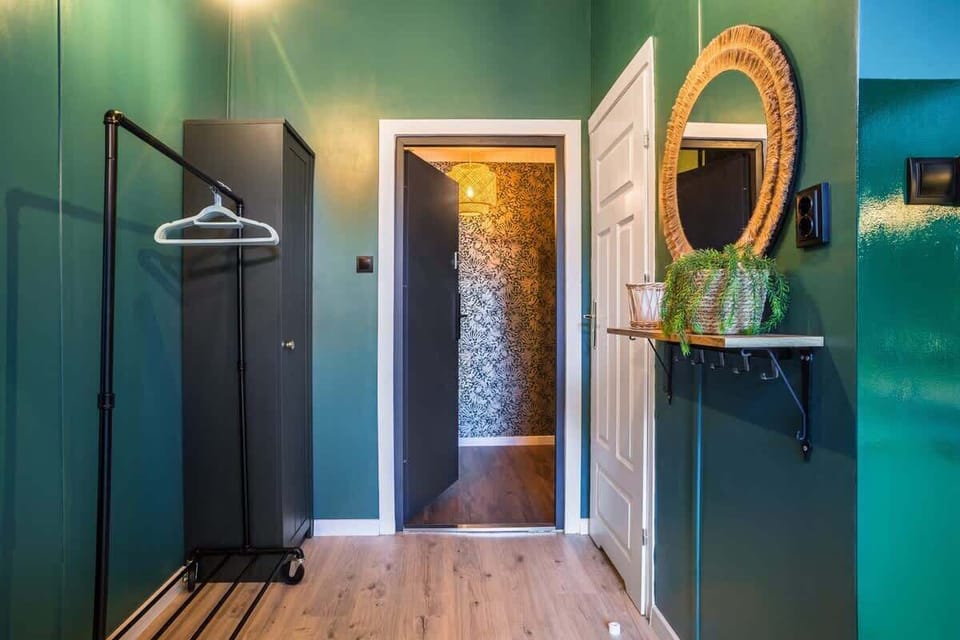 A hallway with a black clothing rack, a patterned door, and warm lighting.

