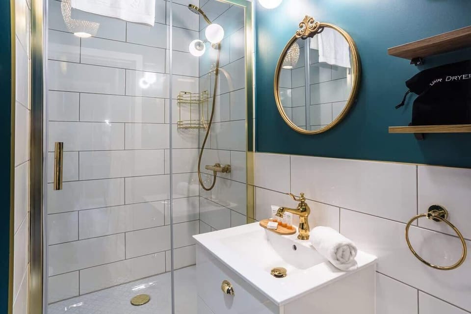 A modern bathroom with gold fixtures, a round mirror, and a glass shower.


