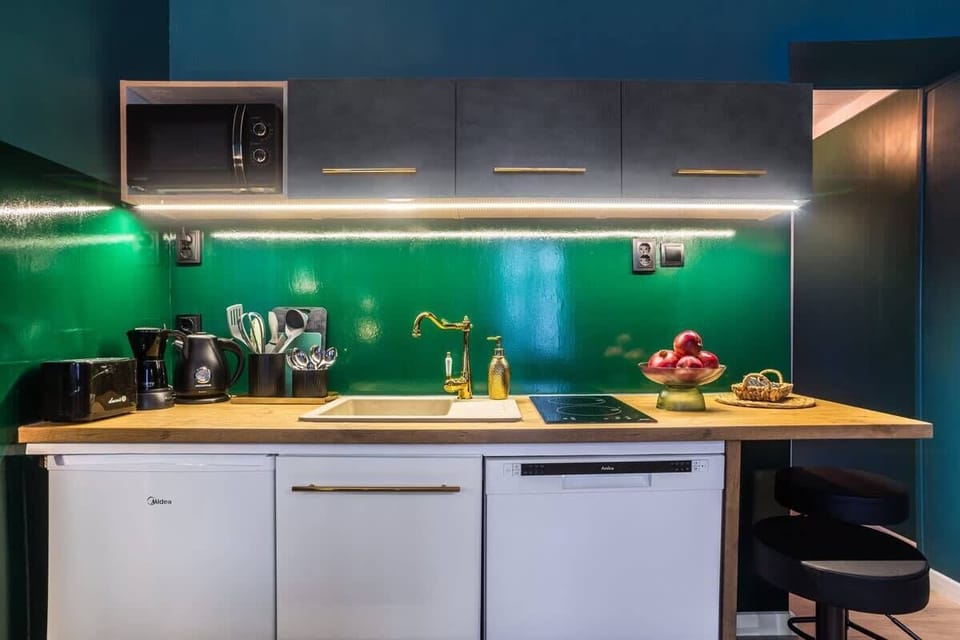 A well-lit kitchen with dark cabinets, gold fixtures, and an elegant backsplash.

