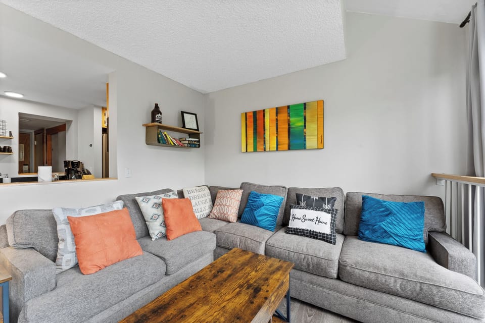 The newly-furnished living area features a queen sleeper sofa, TV, floor-to-ceiling windows, and a wood-burning fireplace.