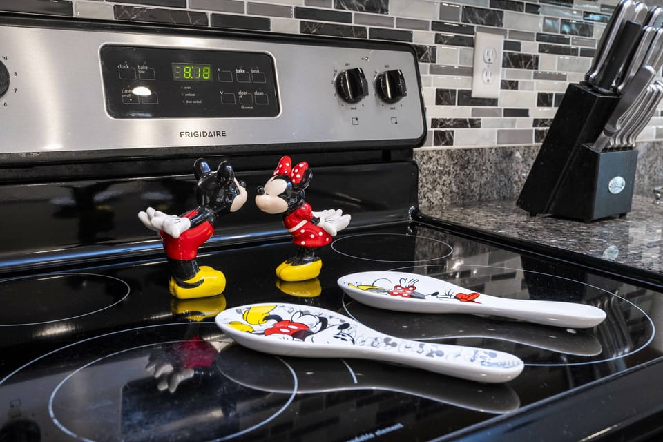 Experience a charming kitchen adorned with whimsical Mickey and Minnie Mouse figurines, sleek black appliances, a striking mosaic backsplash, and glossy countertops, inviting you to gather and embark on culinary adventures.