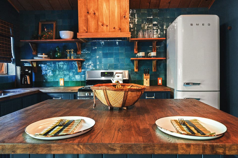 A full kitchen with counter seating includes a Smeg fridge, microwave, gas stove, and all of the dishes, drinkware, and utensils you'll need to make meals or drinks.