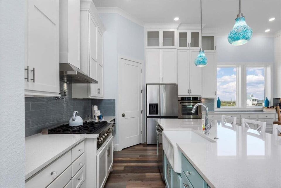 Modern coastal kitchen with gas range, large island, quartz countertops, and abundant cabinet storage for extended stays.