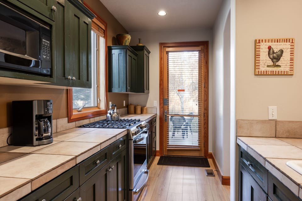 - Fully equipped kitchen with rustic cabinets and tile  
- Stainless steel appliances ready for home cooked meals  
- Window and back door open to fresh mountain air