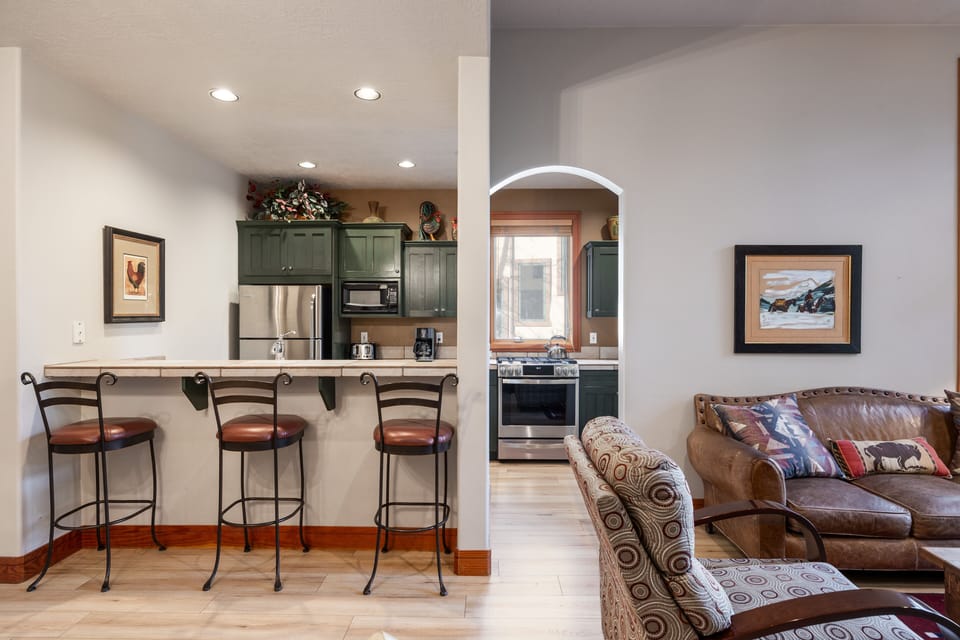 - Kitchen breakfast bar with stools for casual dining  
- View of rustic green cabinets and stainless appliances  
- Open concept connects living space for convenience