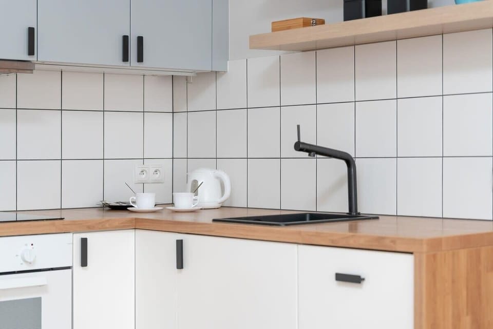 A minimalist kitchen with white and wooden elements, black fixtures, and open shelving.

