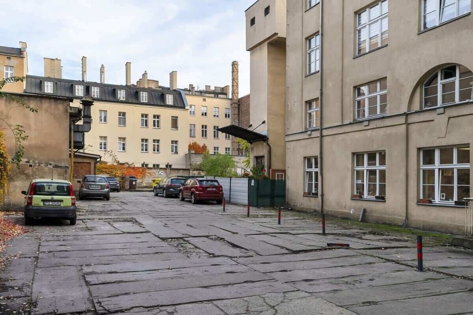 A historic residential courtyard with parked cars, old buildings, and a worn pavement.
