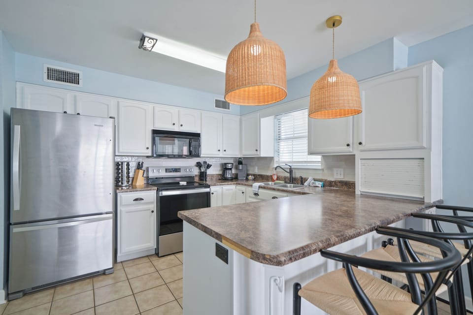 Spacious kitchen with stainless steel appliances, bar seating, and warm coastal lighting—perfect for casual dining and entertaining.