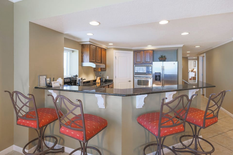 This kitchen features granite countertops, stainless appliances, and a welcoming bar area with red cushioned stools