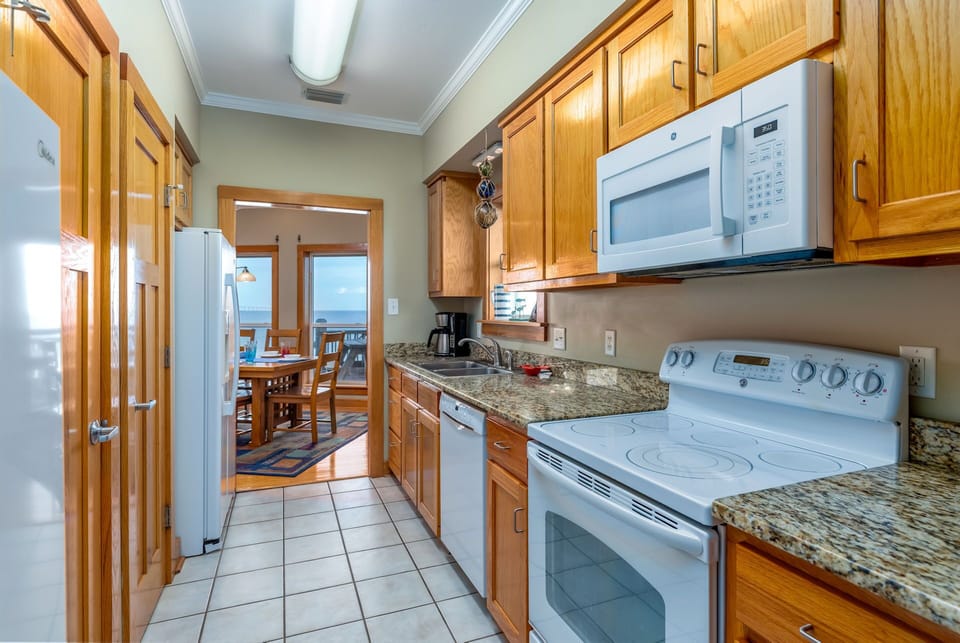 Your fully equipped kitchen features granite counters, modern appliances, and beautiful ocean views through the adjacent dining area.