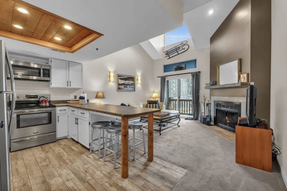 The home features an open and bright living room/kitchen/dining area, with high ceilings and large windows that look towards the ski slopes.