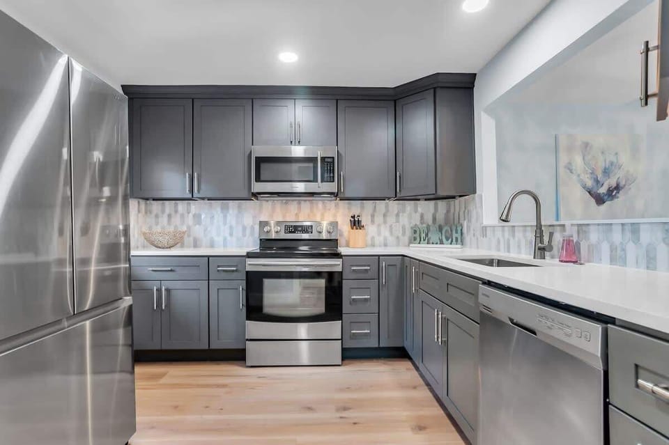 Cook your favorite meals in this fully equipped modern kitchen featuring sleek gray cabinets, stainless steel appliances, and elegant quartz countertops.