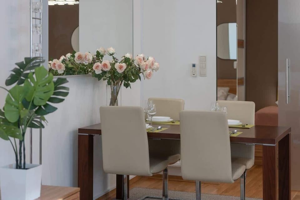 The dining area with fresh flowers in a vase, beige chairs, and a reflective wall feature.
