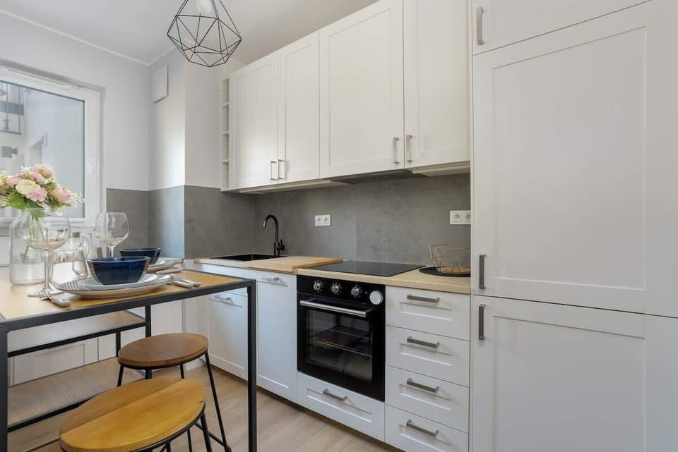 A bright kitchen featuring white cabinets, a built-in oven, and a small dining spot.
