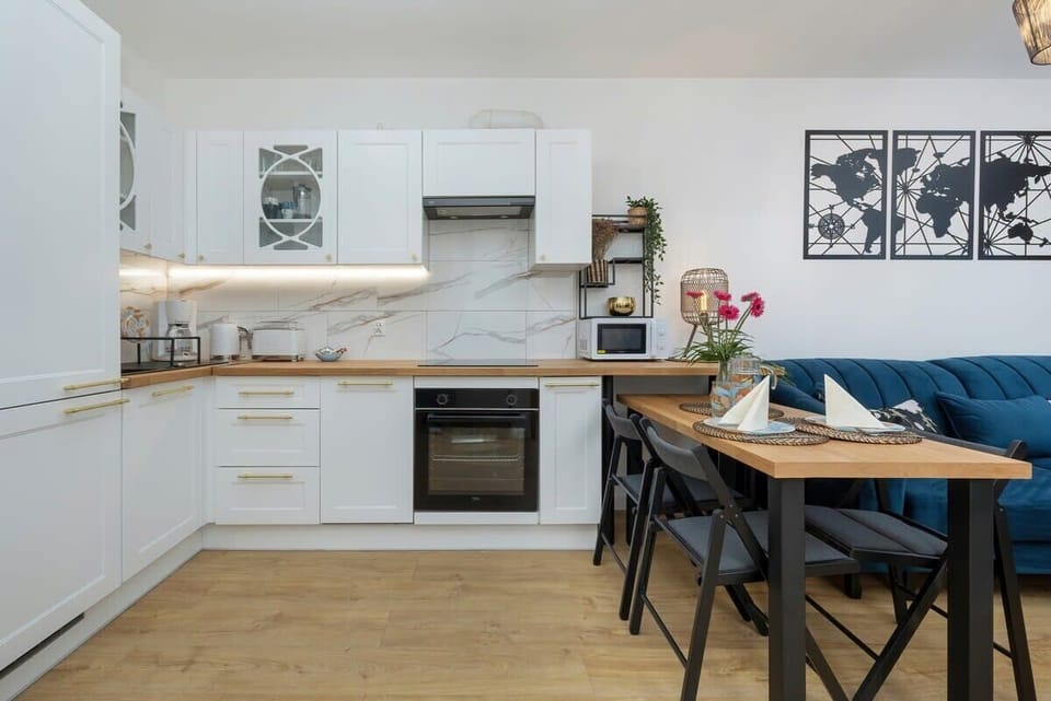 A bright kitchen with white cabinets, wooden countertops, and a dining area.
