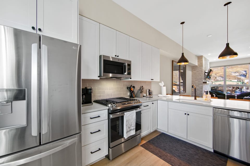 Your fully equipped kitchen features stainless steel appliances, sleek white cabinetry, and mountain views through the window.