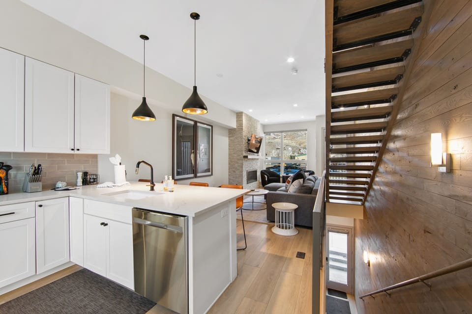 Your modern kitchen flows seamlessly into the living area, featuring sleek white cabinets, pendant lighting, and a stunning wood-accent staircase.