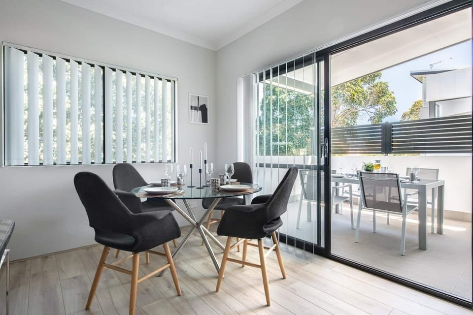 Elegant dining space with a glass-top table, stylish chairs, and access to a sunny balcony.