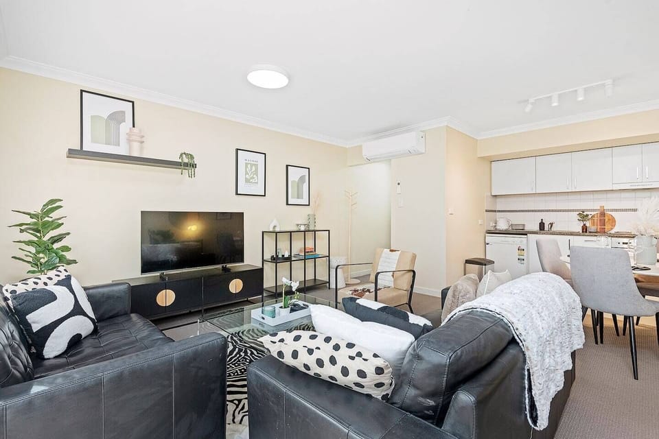 Step into comfort and style in our inviting living area, featuring a plush black leather sofa, modern decor, and a large flat-screen TV for your entertainment. 