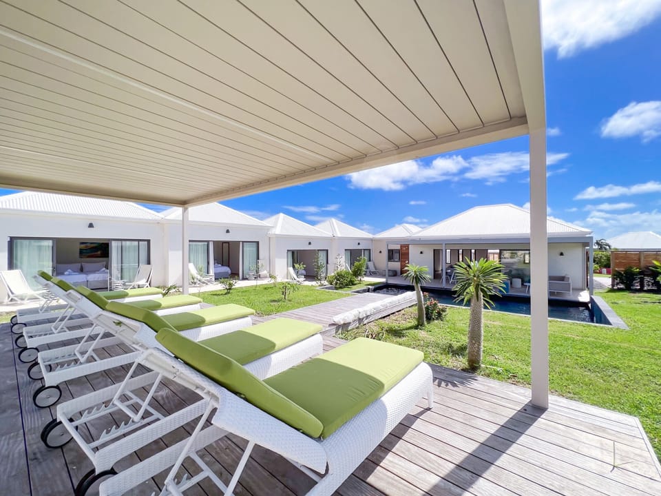Picture showing a row of comfortable loungers with green cushions on a wooden deck, overlooking the pool and the villa.