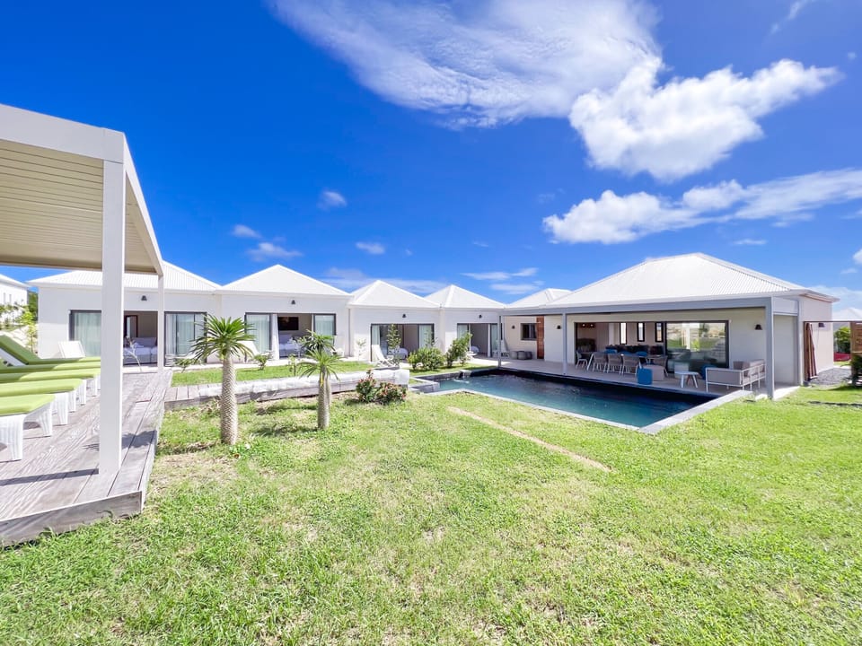 Picture of a modern villa with a lush garden, a rectangular pool, and a living room that opens onto an outdoor terrace.