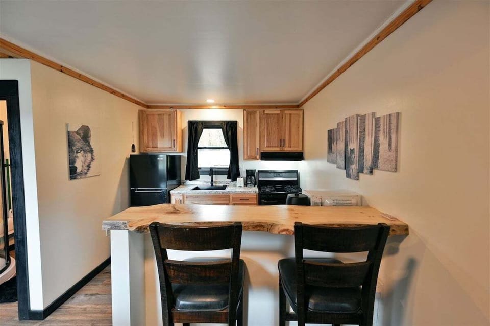 A compact kitchen with light wood cabinets, a black refrigerator and stove, and a live-edge wood breakfast bar with two black chairs.
