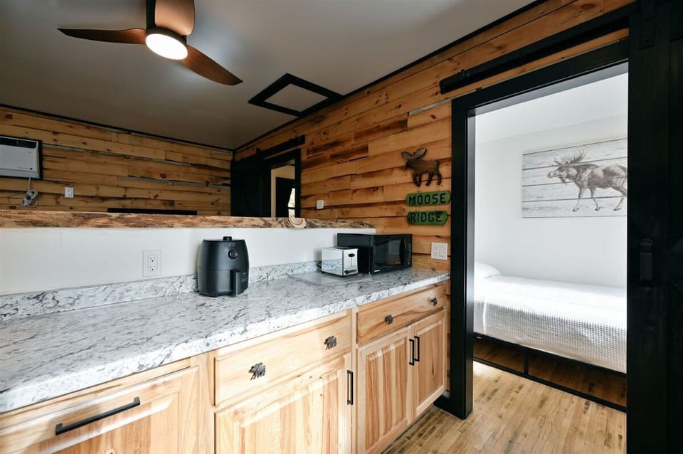 Modern bedroom with a white bed, a moose-themed wall hanging, and a window showing a wooded landscape.