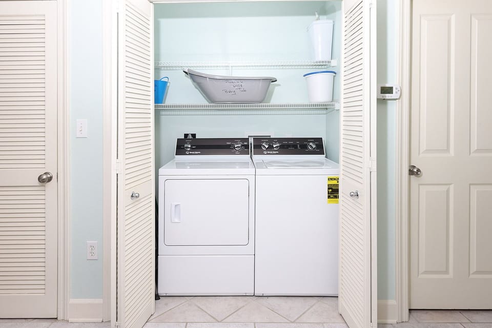 Washer and dryer are neatly arranged in a light blue laundry closet with shelves for storage above