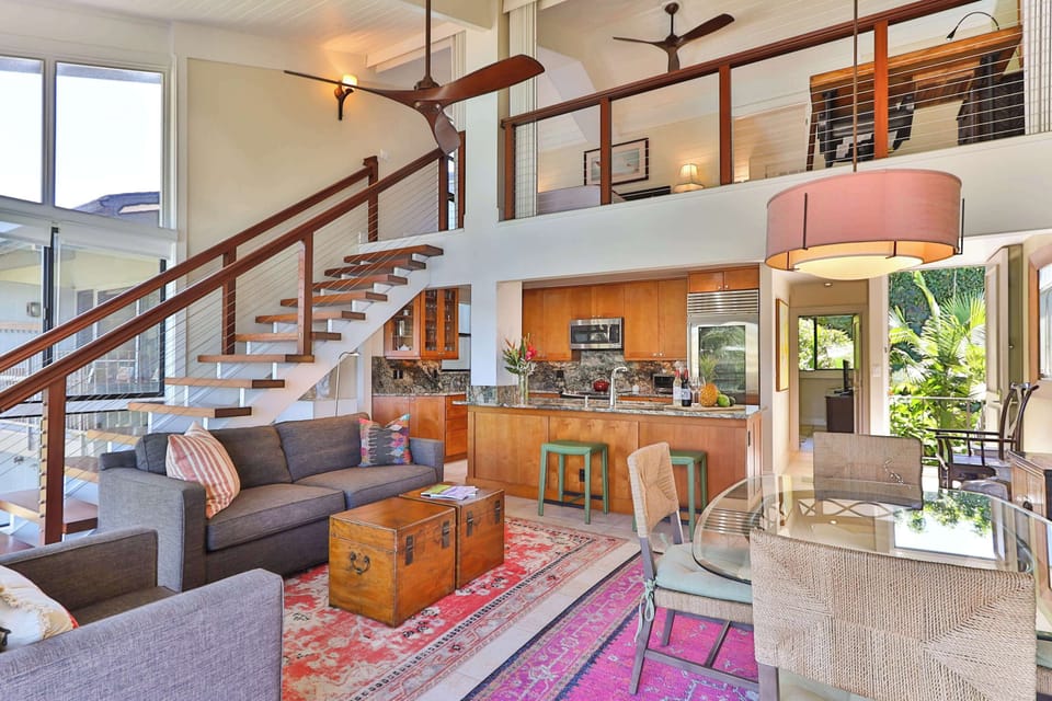 Stylish open-concept living space with vaulted ceilings, modern kitchen, and loft design. Features cozy seating, dining area, and large windows that fill the room with natural light—perfect for relaxing or entertaining in a bright island retreat.