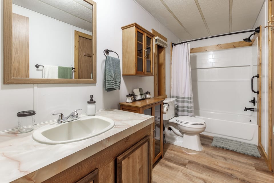 This clean and well-appointed master bathroom offers a full tub/shower combo, plenty of counter space, and rustic cabinetry to complete the cozy cabin feel.