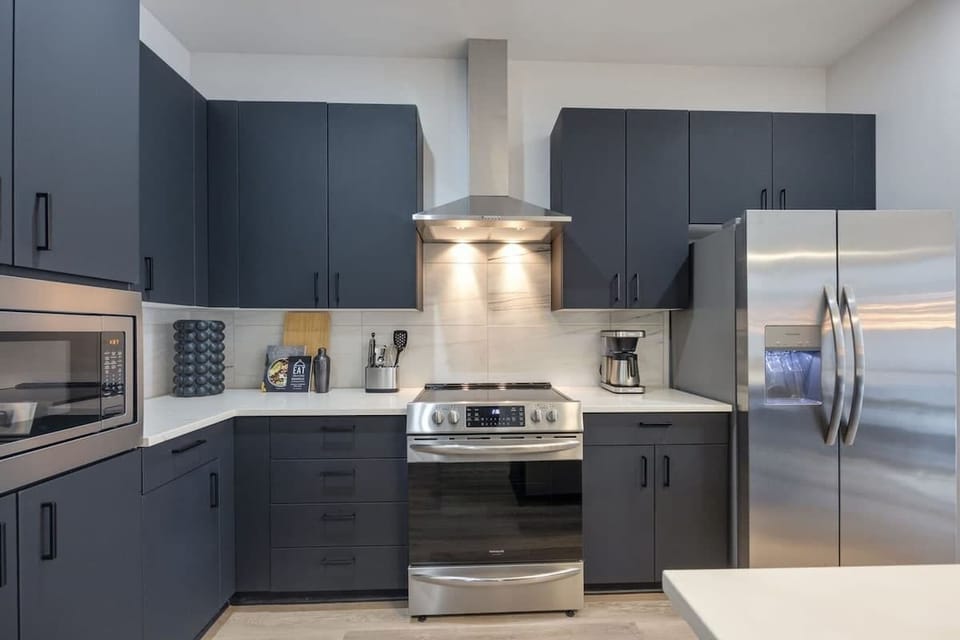 Fully equipped kitchen with stainless steel appliances, basic cooking essentials, toaster, coffee machine, and kitchen island seating.