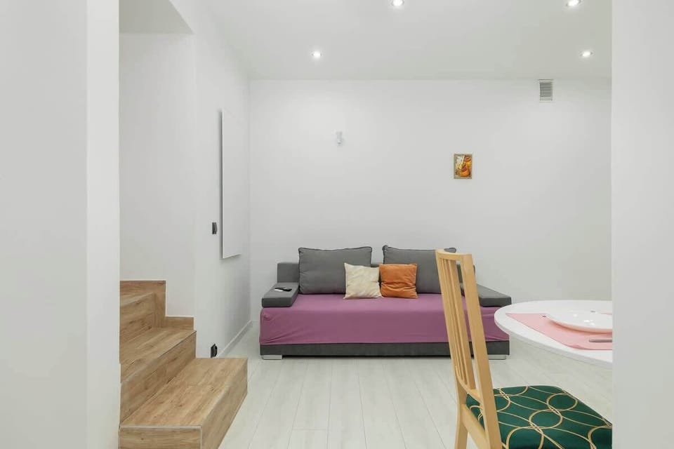 Living room area with a similar setup as in previous images, featuring a white and minimalistic design with a pink sofa and a  dining table.