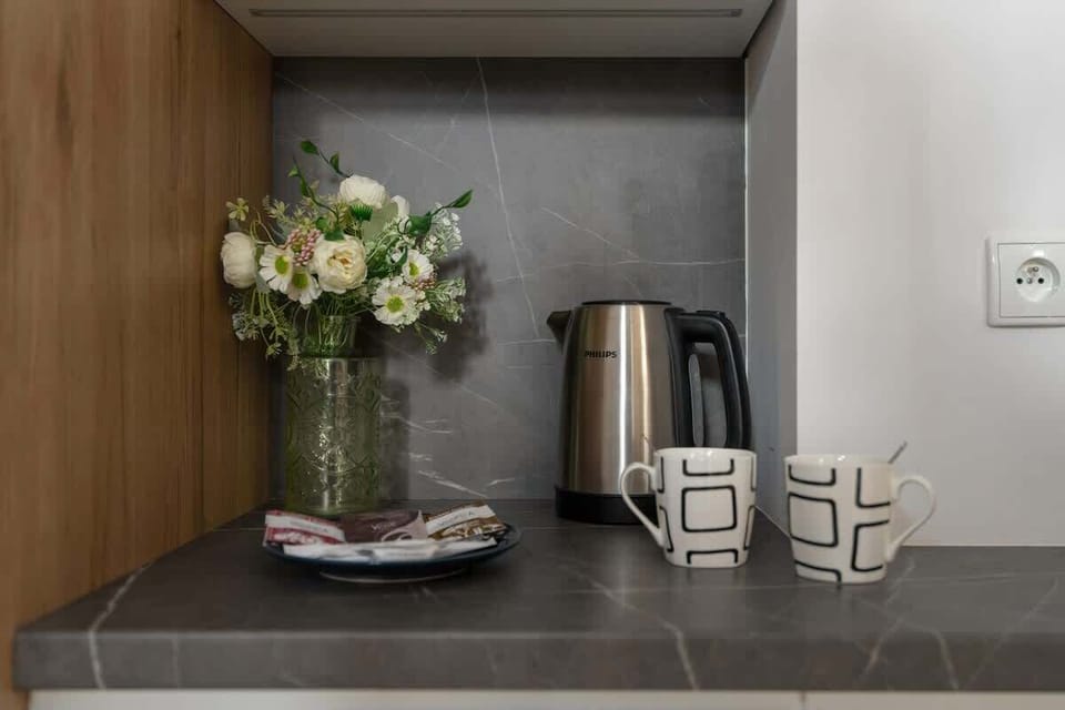 A coffee and tea station on a dark countertop, adorned with fresh flowers and two mugs.
