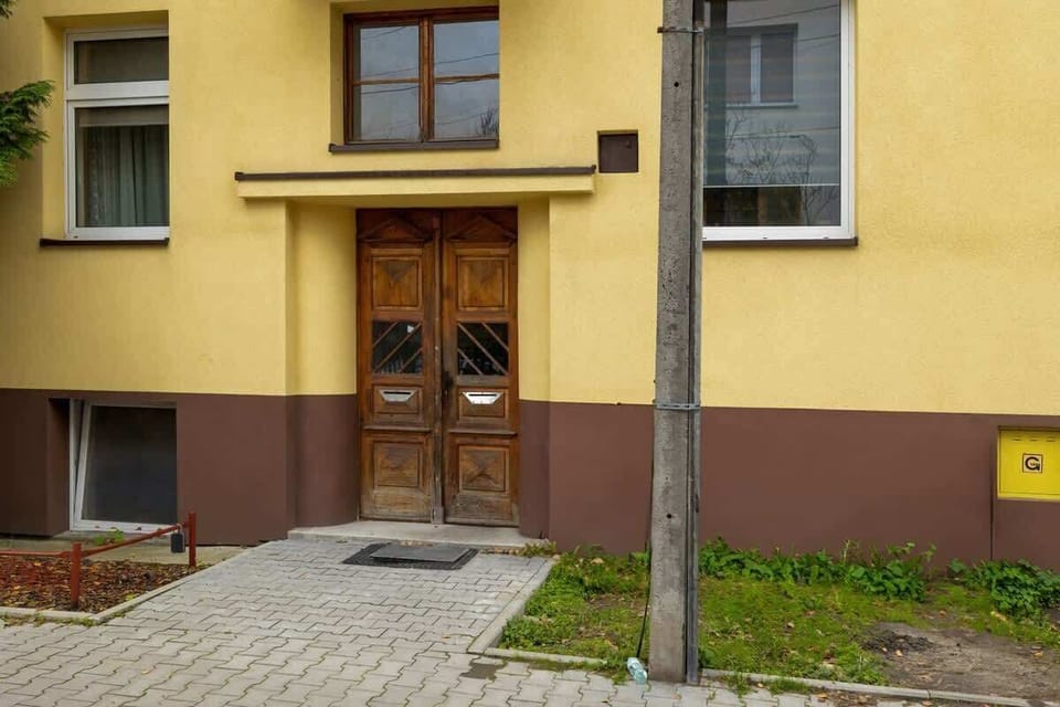 The building's main entrance featuring a classic wooden door, yellow facade, and a small green area near the pathway.
