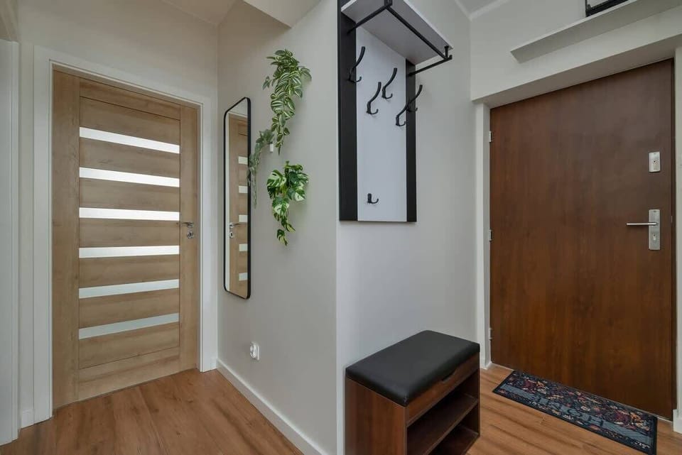 An inviting entrance hall with a modern wooden door, decorative wall art, and hanging plants, creating a welcoming atmosphere.
