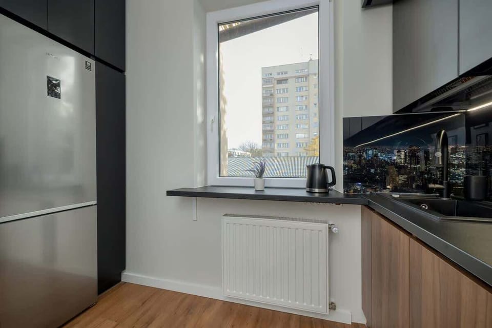A kitchen corner with a bright window, showcasing modern appliances, black backsplash, and ample countertop space.

