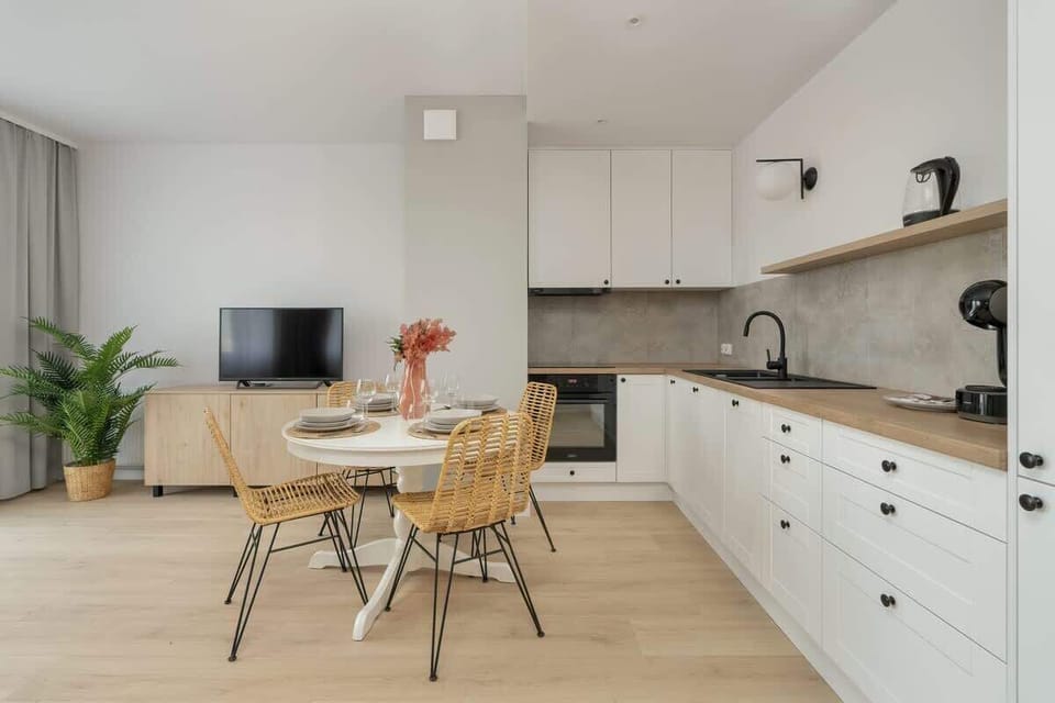 A spacious open-plan kitchen and dining area with white cabinets, wooden countertops, and a chic round dining table with wicker chairs.

