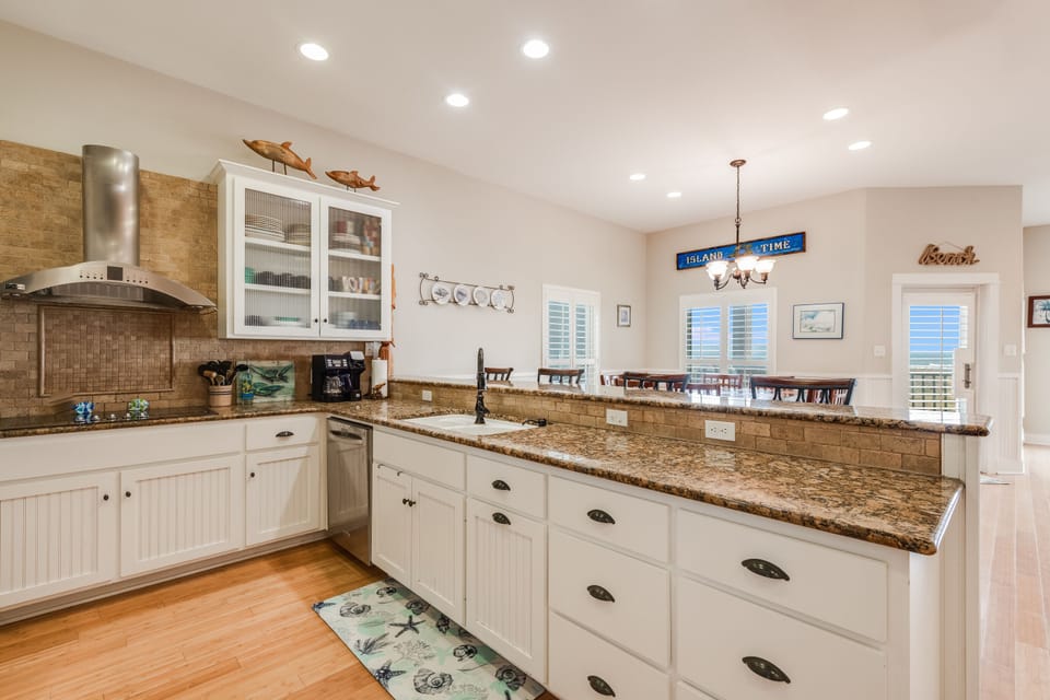 Your fully equipped kitchen features granite countertops, white cabinets, and modern appliances—perfect for preparing meals while enjoying ocean views through the windows.