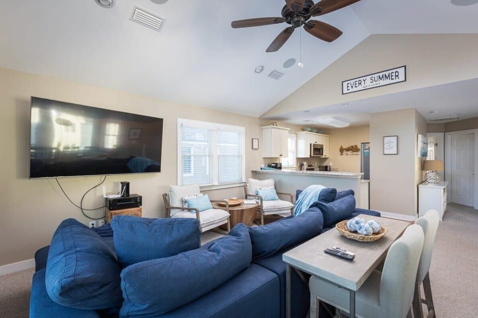 Top Level: Open-concept living area featuring cozy sectional seating, flat-screen TV, expansive windows and sun deck access, plus a convenient bar table with stools.